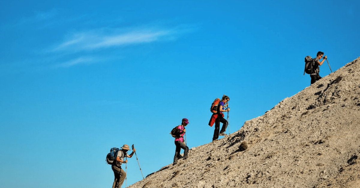 4 hikers walking up a hill agains the blue ski 