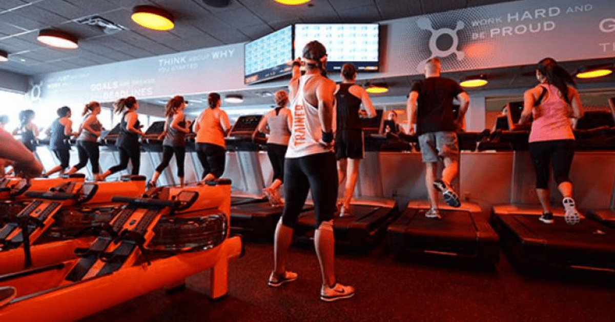 a group running on treadmills in an orange lit room