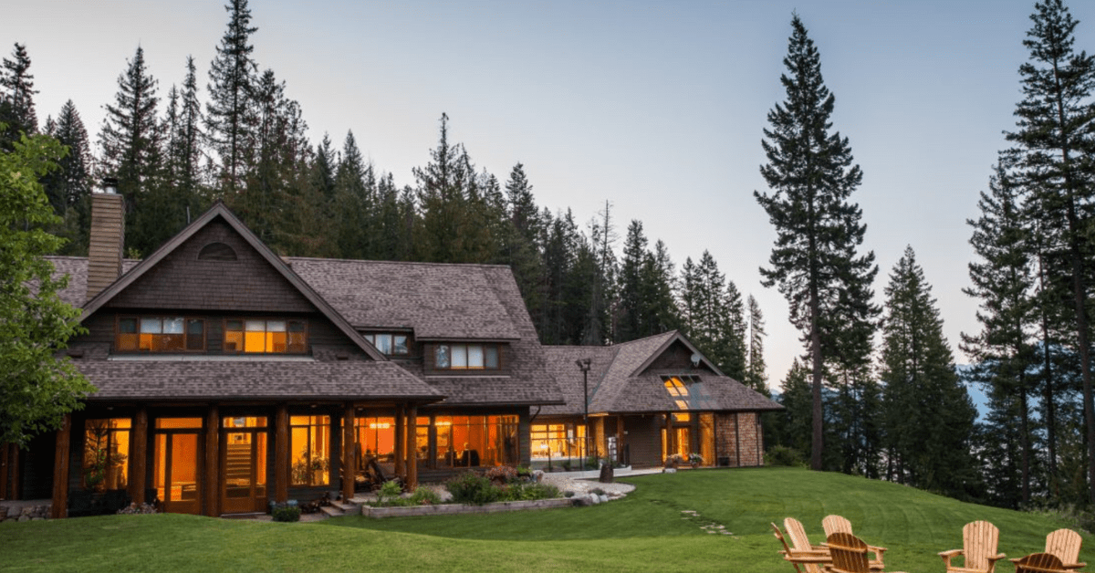 brown house in the woods with some decking chairs in the front garden