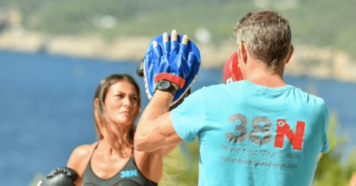 woman punching boxing mitts worn by man in light blue t-shirt