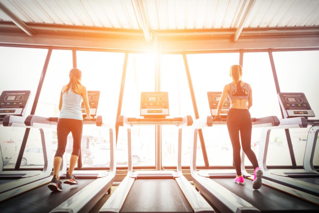 Sport girls running on treadmill in fitness gym at sunrise.